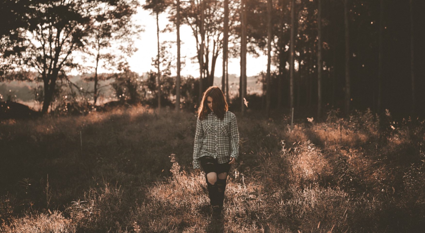 Sepia-tinted photo of woman in plaid shirt walking in forest